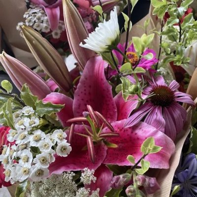 A vibrant bouquet of cut flowers, prominently featuring bold pink lilies and purple coneflowers amongst other blossoms.